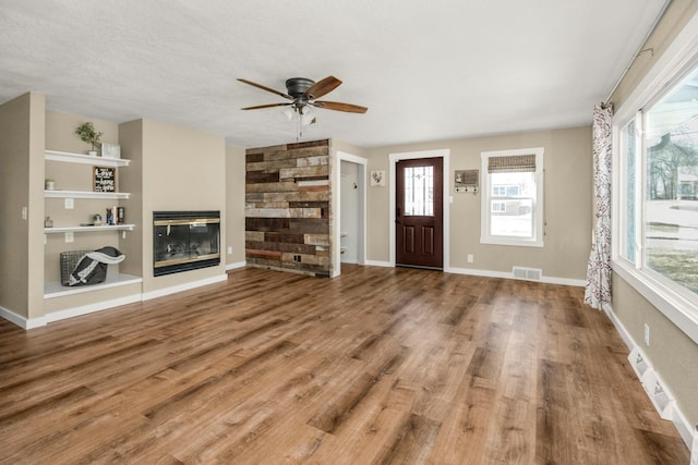 foyer with a glass covered fireplace, wood finished floors, visible vents, and baseboards