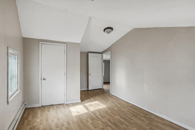 unfurnished bedroom featuring lofted ceiling, light wood-type flooring, a baseboard radiator, and baseboards