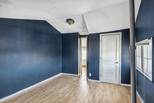 unfurnished bedroom featuring light wood-style flooring, baseboards, and vaulted ceiling