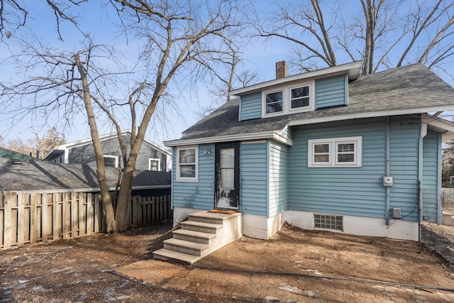 rear view of house featuring roof with shingles, fence, and a chimney