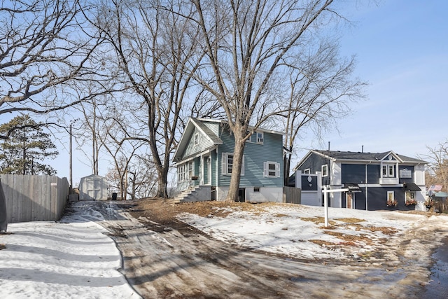 view of snowy exterior with a storage shed, fence, and an outdoor structure