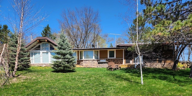 rear view of property featuring stone siding and a yard