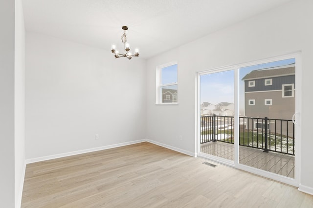 spare room with a chandelier, a wealth of natural light, and light hardwood / wood-style floors