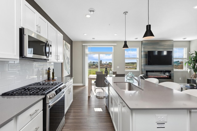 kitchen with sink, white cabinetry, decorative light fixtures, a center island with sink, and stainless steel appliances