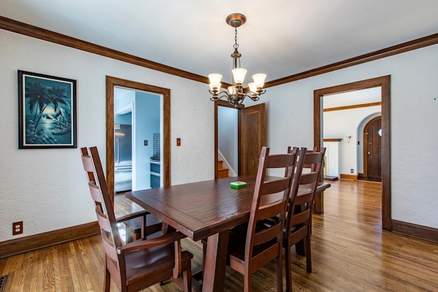 dining room with wood-type flooring, ornamental molding, and an inviting chandelier