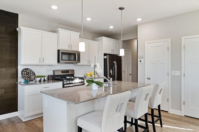 kitchen with light hardwood / wood-style flooring, white cabinetry, stainless steel appliances, an island with sink, and decorative light fixtures