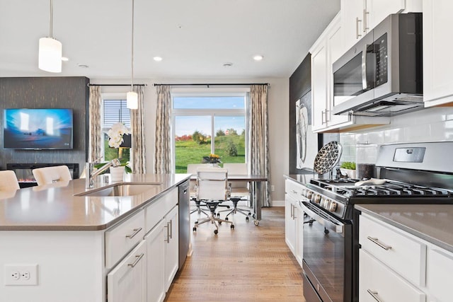 kitchen with decorative light fixtures, white cabinetry, sink, stainless steel appliances, and a center island with sink