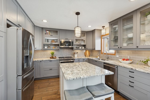 kitchen featuring gray cabinets, stainless steel appliances, a breakfast bar, and pendant lighting