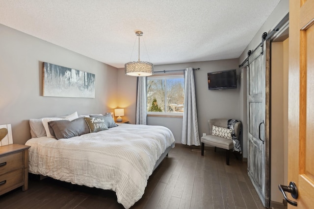 bedroom with a barn door, dark hardwood / wood-style floors, and a textured ceiling