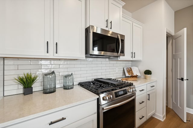 kitchen with decorative backsplash, stainless steel appliances, white cabinets, and light wood-type flooring