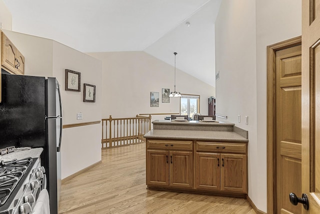 kitchen featuring vaulted ceiling, stainless steel range with gas cooktop, decorative light fixtures, a notable chandelier, and light hardwood / wood-style flooring