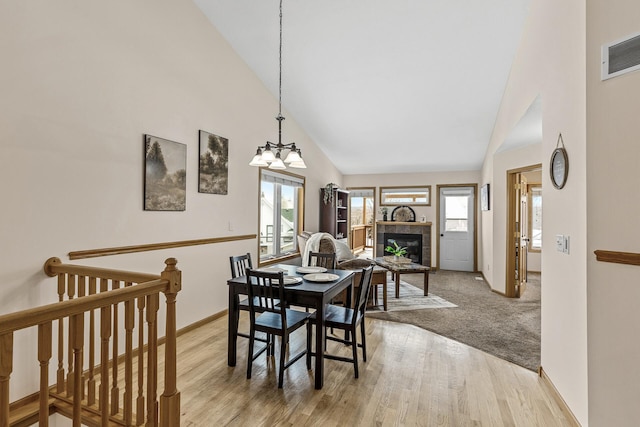 dining room with an inviting chandelier, high vaulted ceiling, a tile fireplace, and light hardwood / wood-style flooring