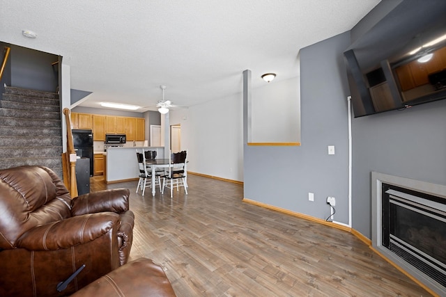 living room featuring ceiling fan, a textured ceiling, and light wood-type flooring