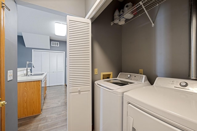 washroom featuring sink, washing machine and clothes dryer, and light hardwood / wood-style flooring