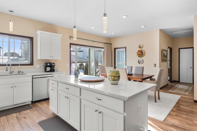 kitchen with sink, light stone counters, white cabinetry, stainless steel dishwasher, and hanging light fixtures