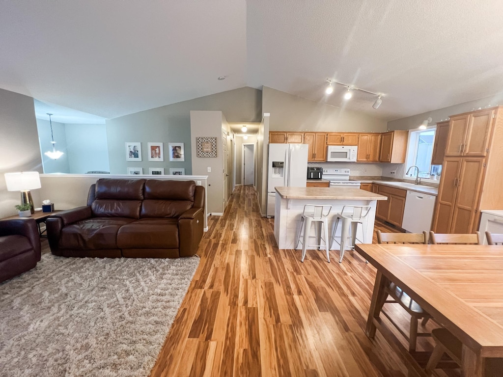 kitchen featuring white appliances, a kitchen breakfast bar, a center island, vaulted ceiling, and light wood-type flooring