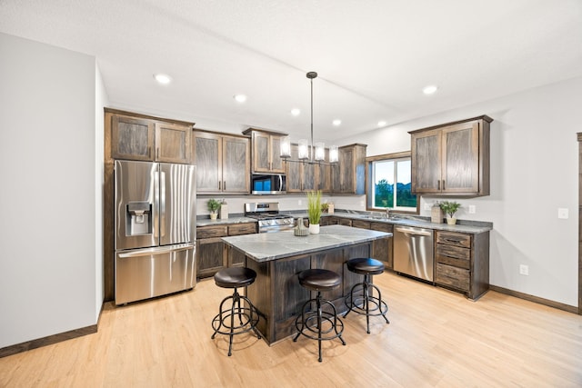 kitchen with decorative light fixtures, a kitchen breakfast bar, a center island, light hardwood / wood-style floors, and stainless steel appliances