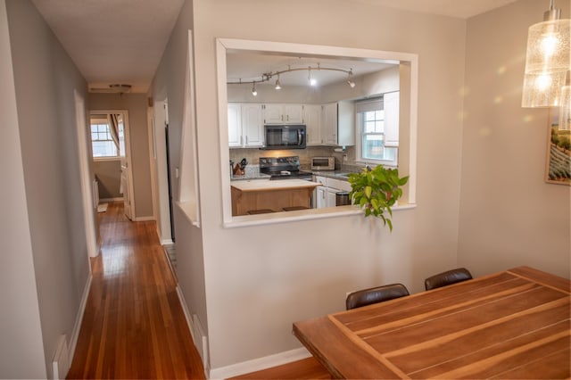 kitchen with decorative light fixtures, electric range oven, kitchen peninsula, decorative backsplash, and white cabinets