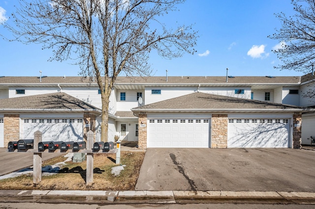 townhome / multi-family property with a shingled roof, stone siding, driveway, and an attached garage