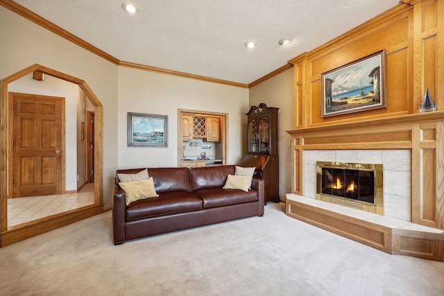 carpeted living room featuring crown molding, a tiled fireplace, and a textured ceiling