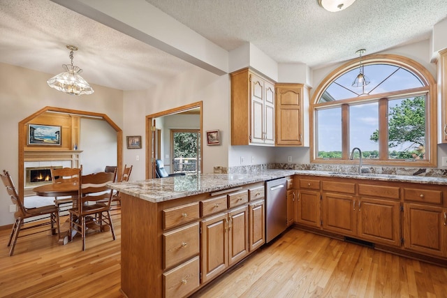 kitchen with sink, light wood-type flooring, stainless steel dishwasher, kitchen peninsula, and pendant lighting