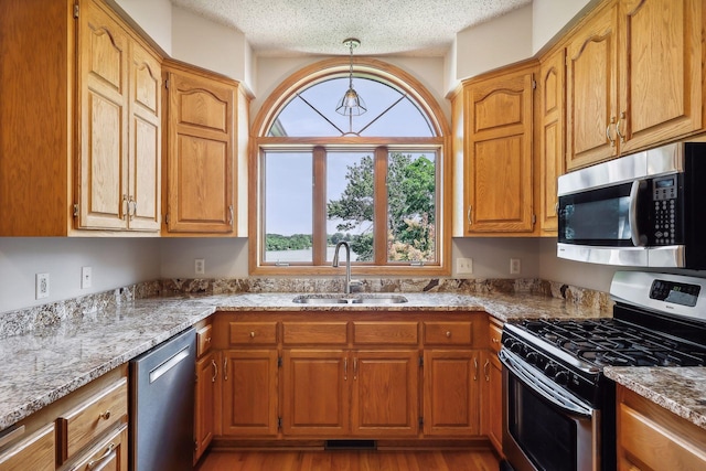 kitchen featuring pendant lighting, stainless steel appliances, light stone countertops, and sink