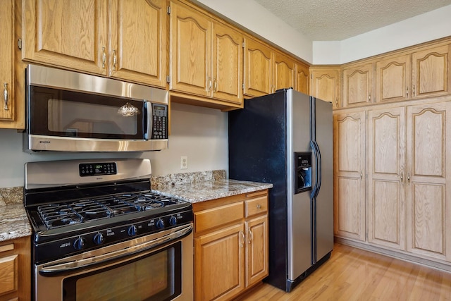 kitchen with light stone countertops, stainless steel appliances, a textured ceiling, and light wood-type flooring