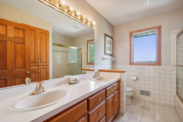 bathroom with toilet, a textured ceiling, tile walls, vanity, and tile patterned flooring