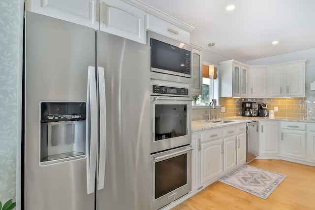 kitchen with white cabinetry, sink, backsplash, stainless steel appliances, and light stone countertops