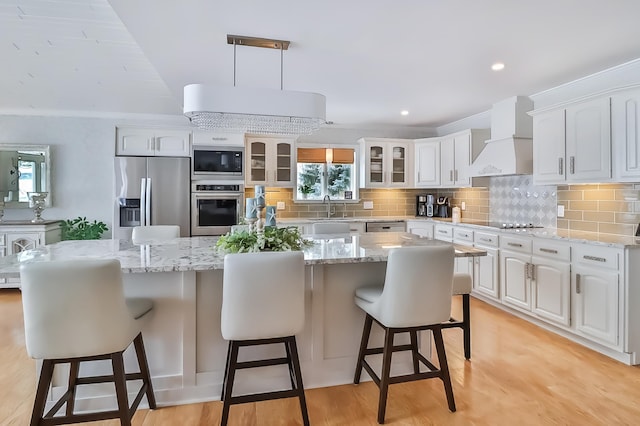 kitchen featuring appliances with stainless steel finishes, white cabinetry, backsplash, a kitchen island, and custom exhaust hood