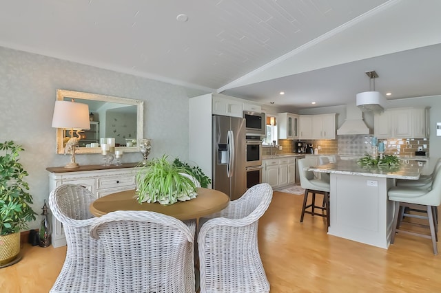 dining room with vaulted ceiling, crown molding, and light wood-type flooring