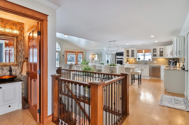 hallway featuring vaulted ceiling, ornamental molding, sink, and light hardwood / wood-style floors