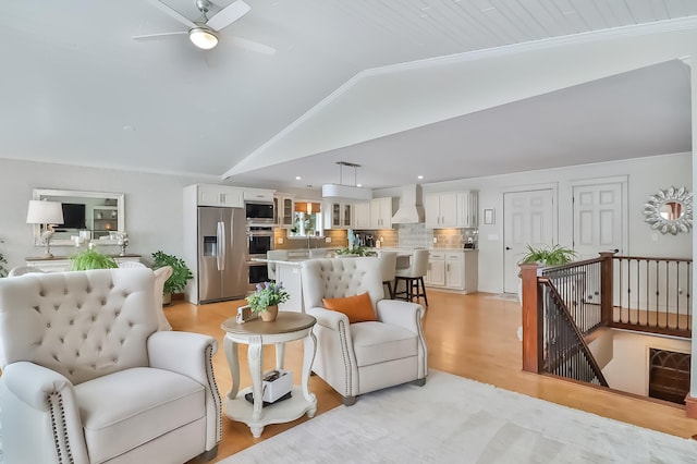 living room with ceiling fan, vaulted ceiling, and light wood-type flooring