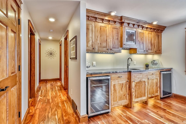 kitchen with sink, dark stone countertops, beverage cooler, and light wood-type flooring