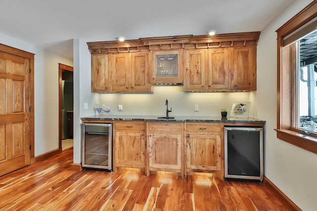 kitchen with hardwood / wood-style floors, dishwasher, sink, beverage cooler, and dark stone counters