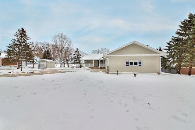 snow covered back of property with a porch and a storage unit