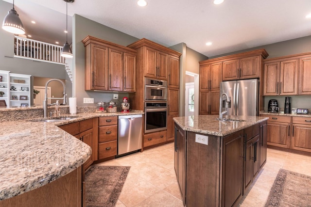 kitchen featuring decorative light fixtures, an island with sink, sink, light stone counters, and stainless steel appliances