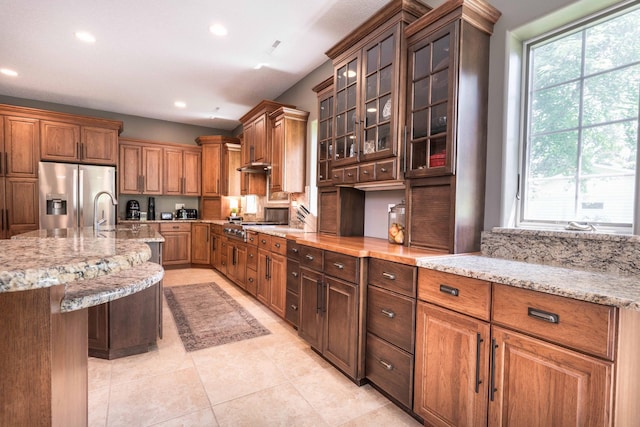 kitchen with appliances with stainless steel finishes, a kitchen bar, light tile patterned floors, light stone counters, and a center island with sink