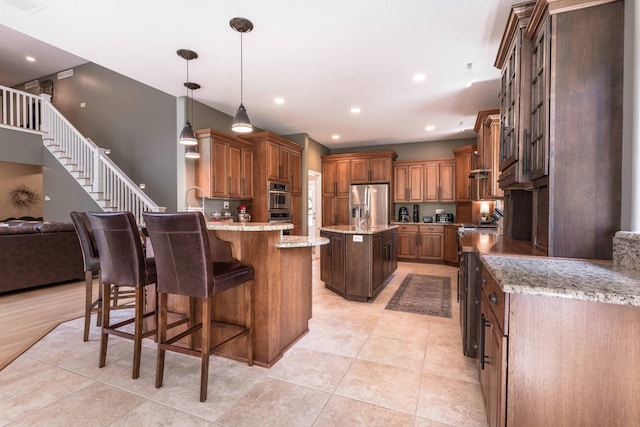 kitchen with appliances with stainless steel finishes, a kitchen island with sink, a kitchen breakfast bar, light stone counters, and decorative light fixtures