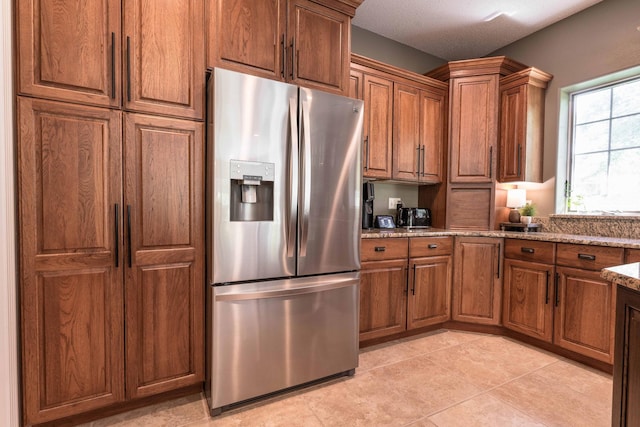 kitchen featuring light stone countertops, stainless steel fridge with ice dispenser, and light tile patterned floors