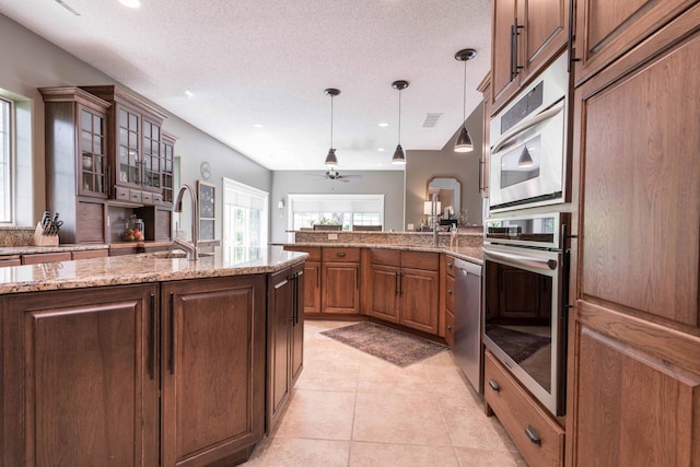 kitchen featuring sink, light stone counters, light tile patterned floors, pendant lighting, and stainless steel appliances