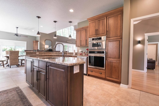 kitchen with pendant lighting, sink, appliances with stainless steel finishes, light stone countertops, and a center island with sink