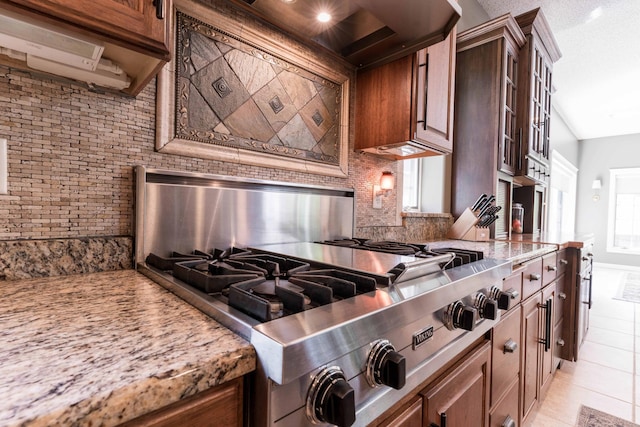 kitchen featuring light tile patterned flooring, stainless steel gas cooktop, light stone counters, brick wall, and decorative backsplash