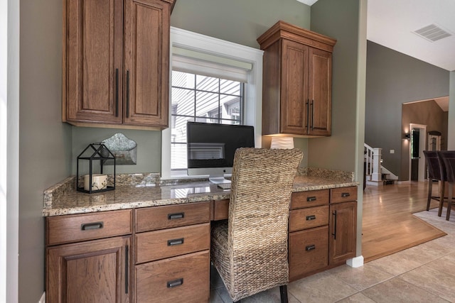 kitchen with light tile patterned flooring, lofted ceiling, light stone countertops, and built in desk