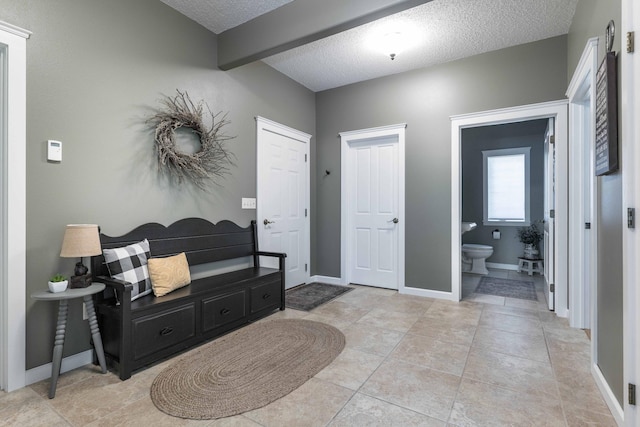 tiled entryway featuring beamed ceiling and a textured ceiling