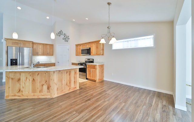 kitchen with sink, appliances with stainless steel finishes, hanging light fixtures, light hardwood / wood-style floors, and a center island with sink