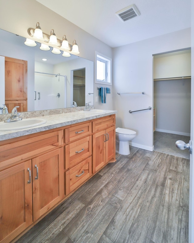 bathroom featuring a shower stall, double vanity, wood finished floors, toilet, and a walk in closet