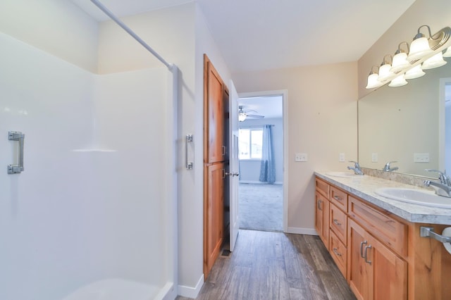 bathroom with a shower, wood finished floors, double vanity, and baseboards