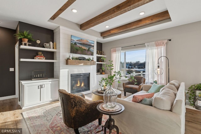 living room featuring beamed ceiling, wood-type flooring, and a large fireplace