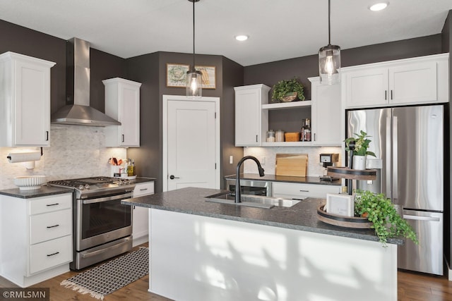 kitchen with appliances with stainless steel finishes, pendant lighting, an island with sink, sink, and wall chimney exhaust hood